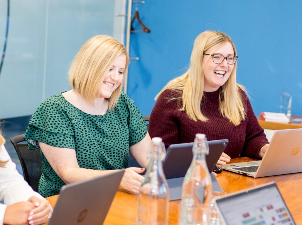 Two smiling females working on laptops at a table